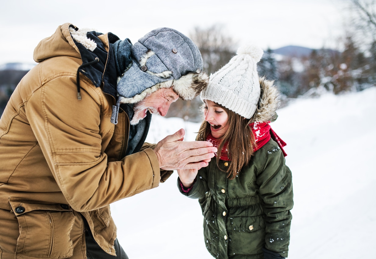Grandfather warming hands of a small girl in snowy nature on a winter day.