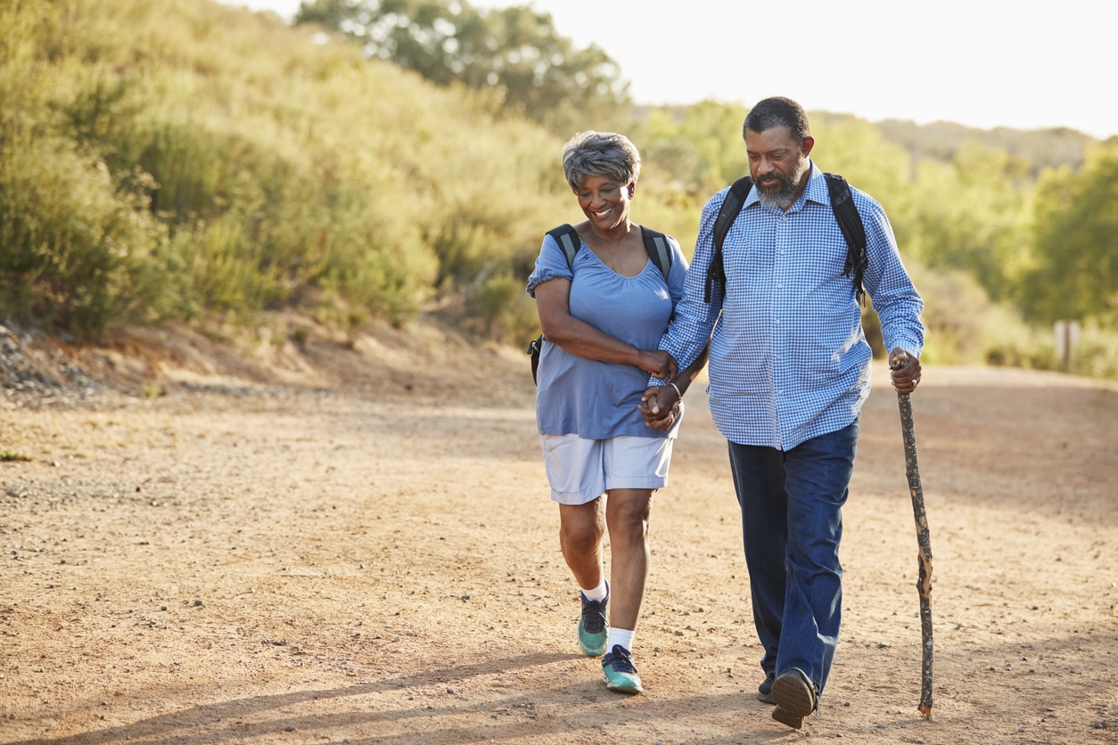 Senior Couple Wearing Backpacks Hiking In Countryside Together