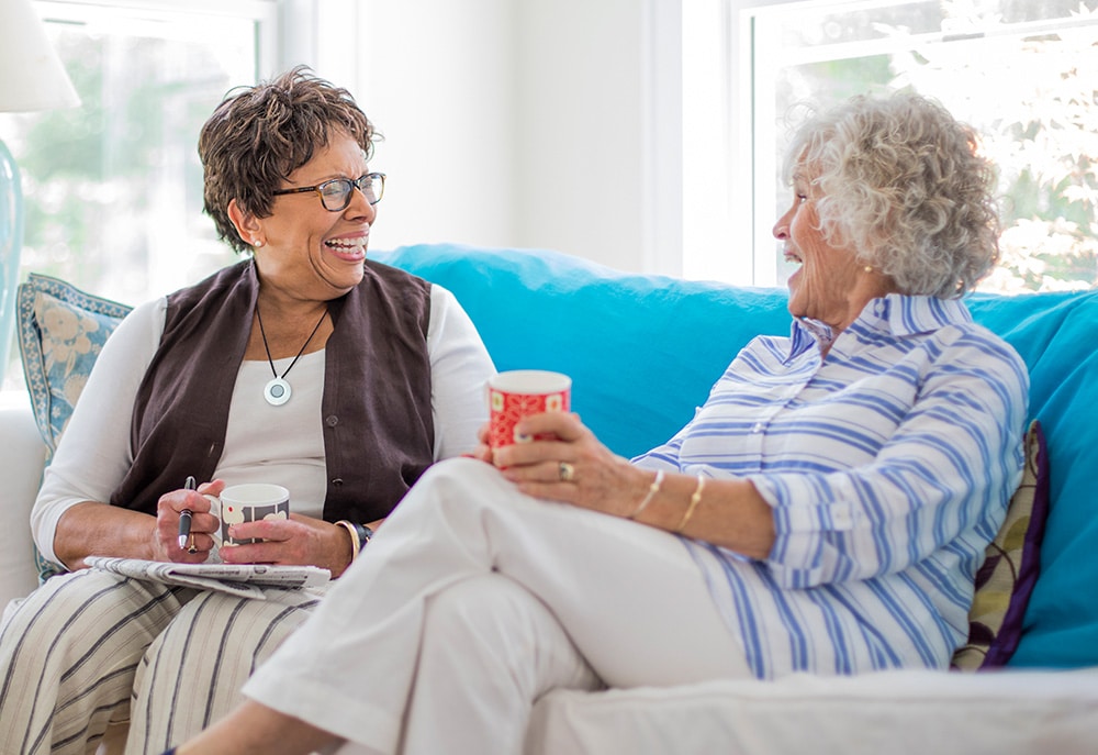 Woman wearing HomeSafe medical alert system sitting on couch with friend