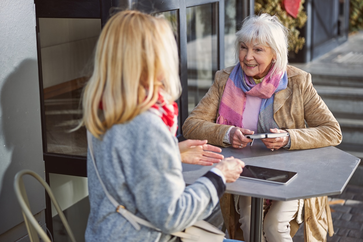 Happy ladies sitting at the restaurant terrace and talking together about good autumn weather.