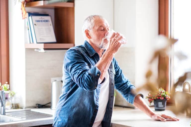 Older man drinking water in his kitchen