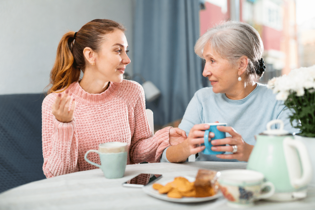 Adult daughter talking with her mother at a kitchen table in warm daylight
