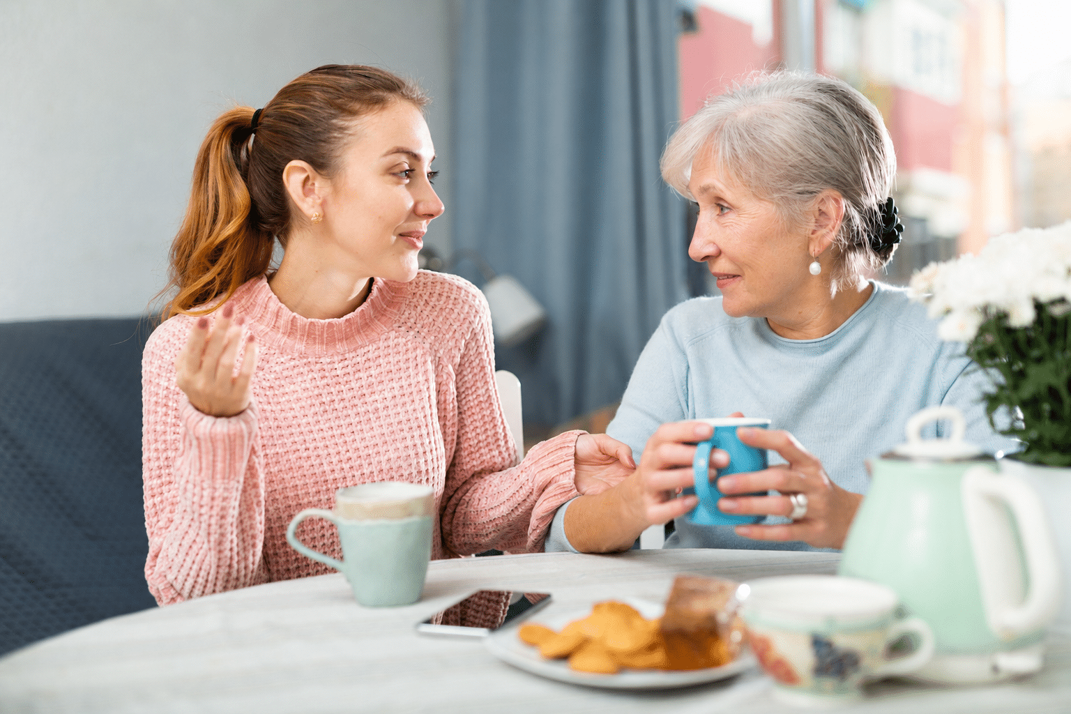 Adult daughter talking with her mother at a kitchen table in warm daylight
