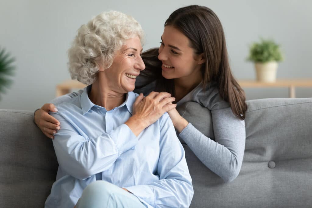 Older woman smiling with her adult daughter at home, highlighting family support and caregiver resources for seniors.