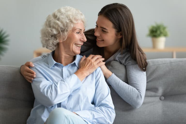 Older woman smiling with her adult daughter at home, highlighting family support and caregiver resources for seniors.