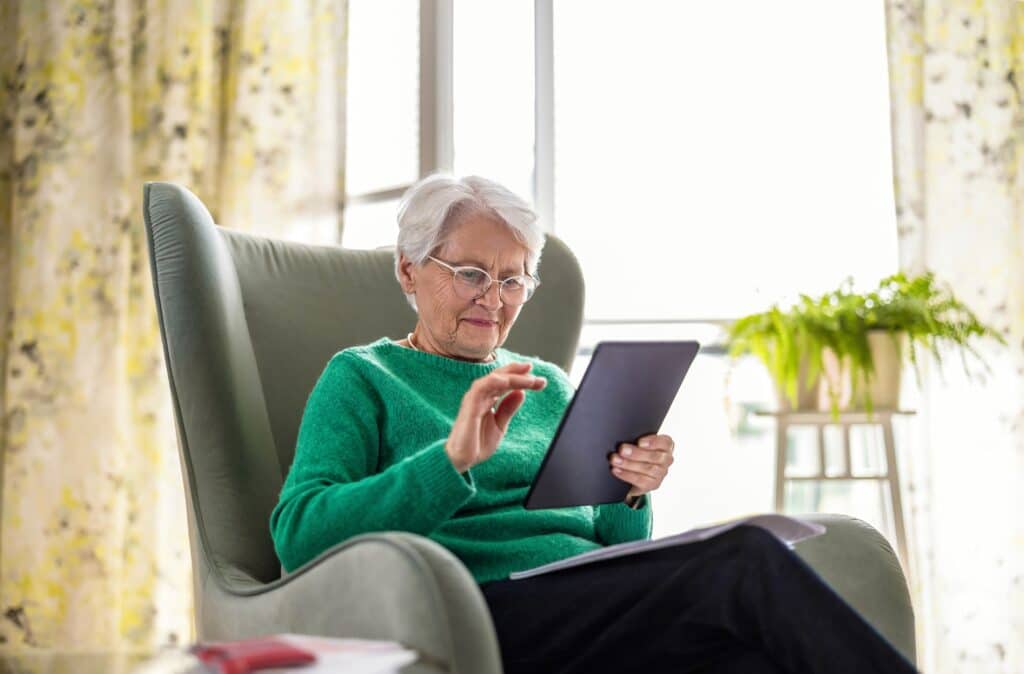 Senior woman using a tablet at home while researching Medicare coverage for medical alert systems.