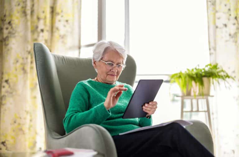 Senior woman using a tablet at home while researching Medicare coverage for medical alert systems.